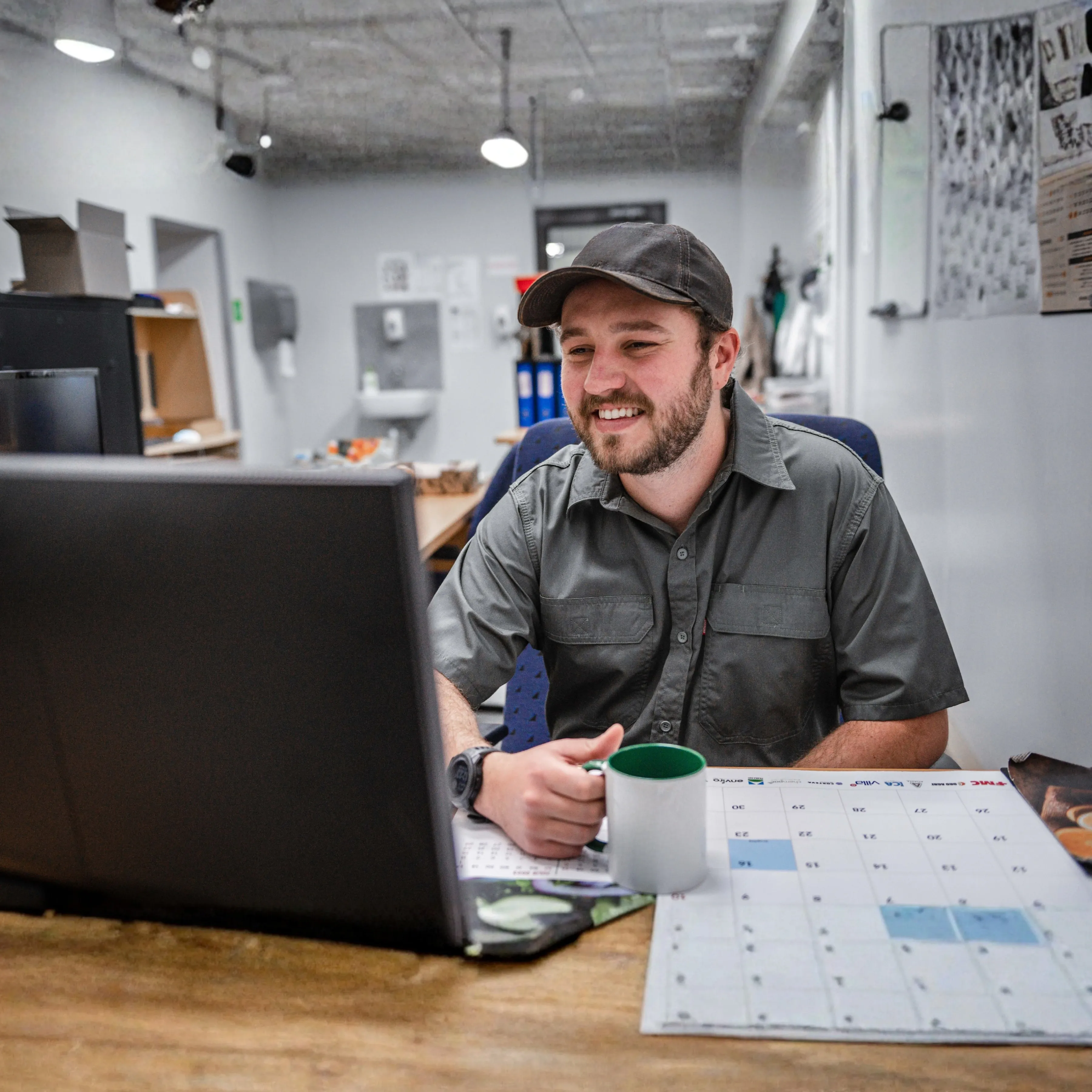 Payroll admin or manager smiling while working at a laptop in an office with a calendar on the desk